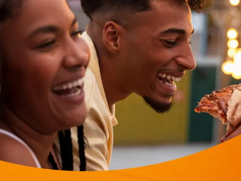 Amigos riendo mientras comen pizza, en la campaña de los 50 años de HOT